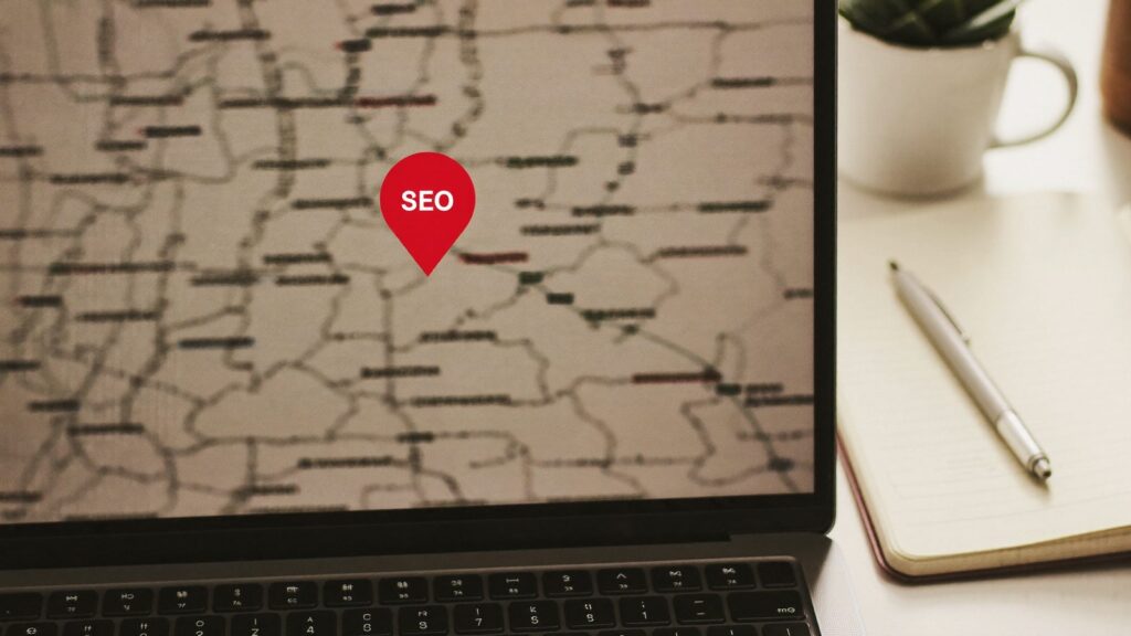 Laptop z mapą i pinezką lokalizacji obok notatnika